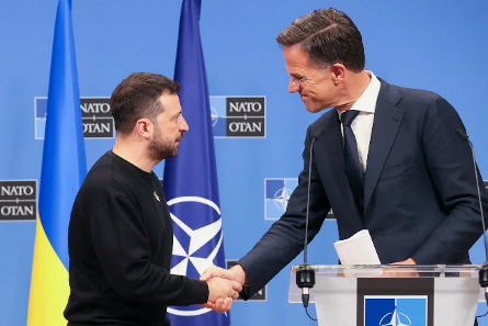 Ukrayna Devlet Başkanı Volodimir Zelenski ve Hollanda Başbakanı Mark Rutte (veya NATO yetkilisi) NATO bayrakları önünde el sıkışırken.