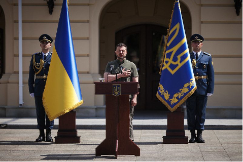 Ukrayna Devlet Başkanı Volodimir Zelenski, ulusal bayraklar önünde elini kalbine koyarak ulusal egemenlik hakkında konuşma yapıyor.