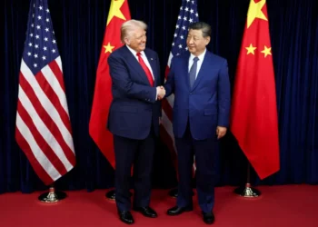 Donald Trump and Xi Jinping shaking hands in front of US and Chinese flags, symbolizing the shift in the 2026 National Defense Strategy
