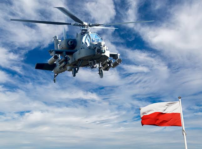 Poland NATO defence: An AH-64E Apache Guardian attack helicopter in flight with the Polish flag, representing Varshava's modernization and military procurement from the US.