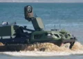 Rheinmetall REPMUS26 görseli: suda ilerleyen, üzerinde sensör direği ve insansız hava aracı bulunan paletli araç.