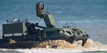 Rheinmetall REPMUS26 görseli: suda ilerleyen, üzerinde sensör direği ve insansız hava aracı bulunan paletli araç.