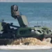 Rheinmetall REPMUS26 görseli: suda ilerleyen, üzerinde sensör direği ve insansız hava aracı bulunan paletli araç.